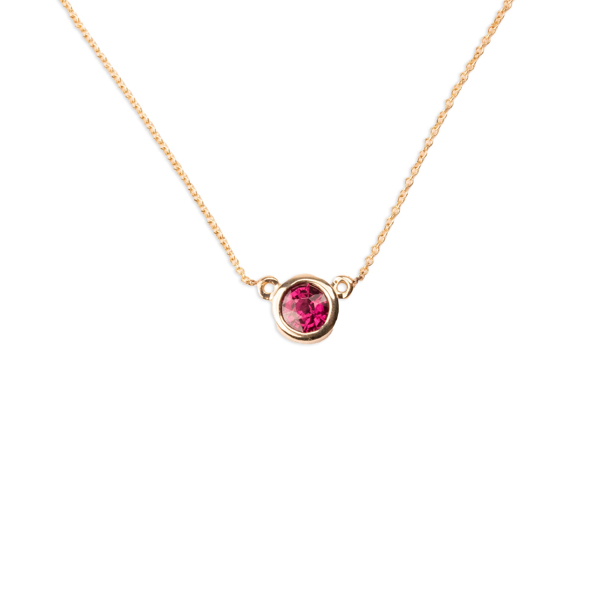 The 14k Garnet Bezel Necklace features a single round, ethically sourced garnet set in a simple gold bezel on a delicate 14k gold chain, shown against a white background.