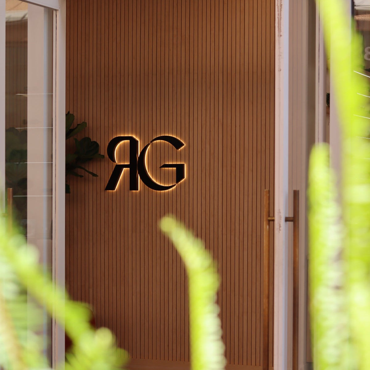 Building facade at Irvine Spectrum Center with RG logo on a wooden slat panel, surrounded by greenery.