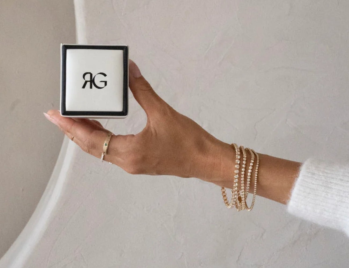 RG ring box held by a wrist stacked with tennis bracelets